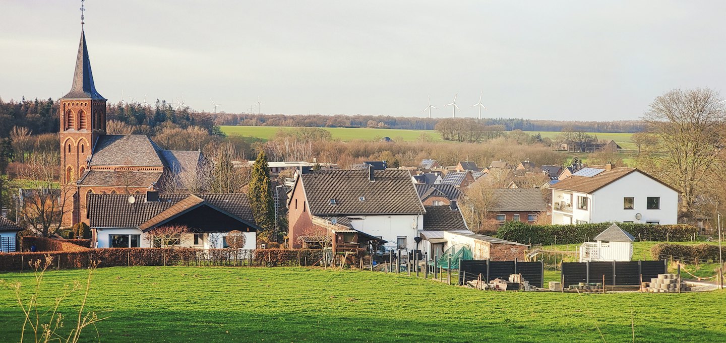 Dorp in een groene vallei met kerk en windmolens.